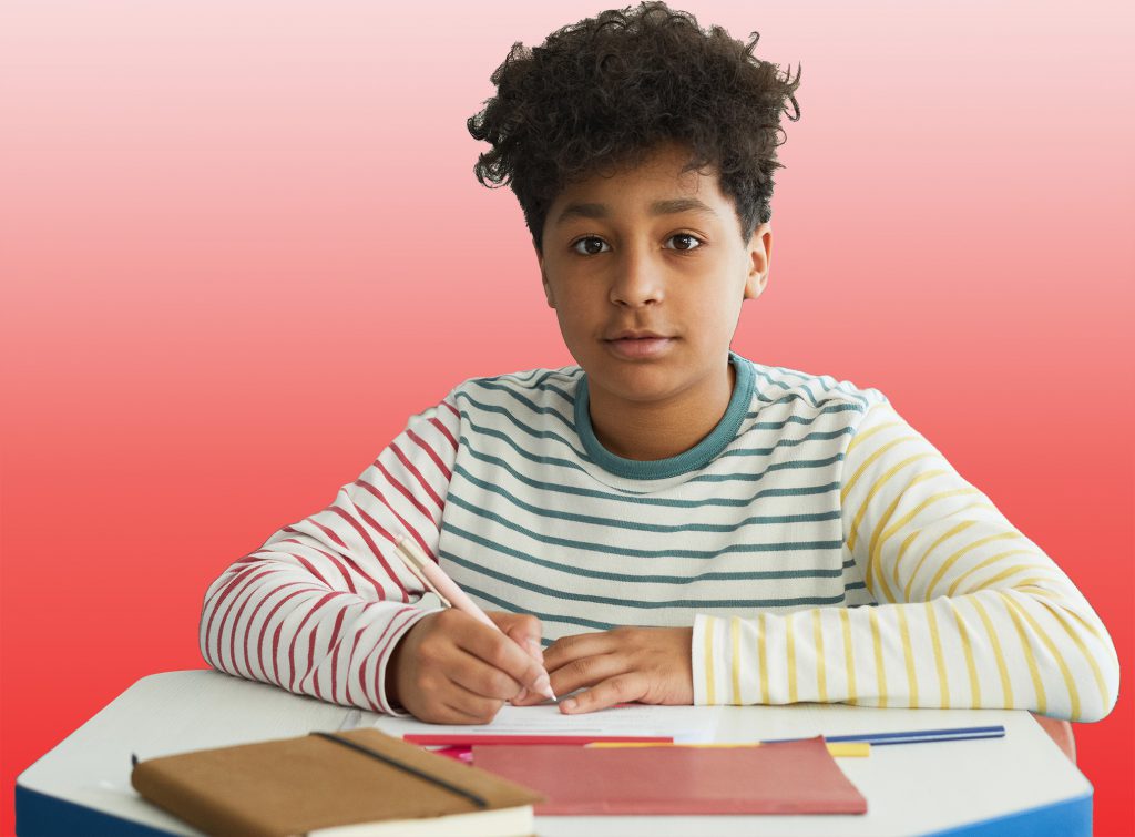 Photo of a boy in a striped shirt sitting at a desk.