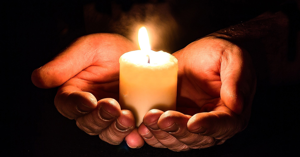 Photo of two cupped hands holding a votive candle.