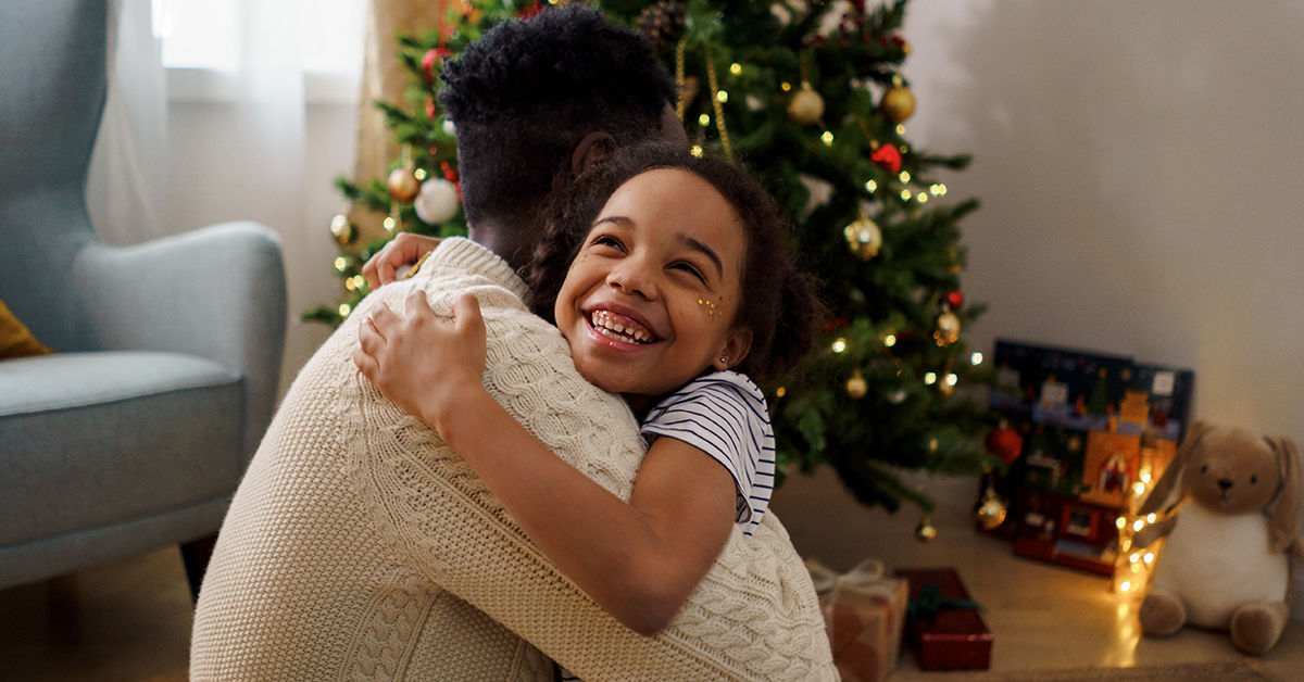 photo of a dad hugging his daughter in front of a Christmas tree